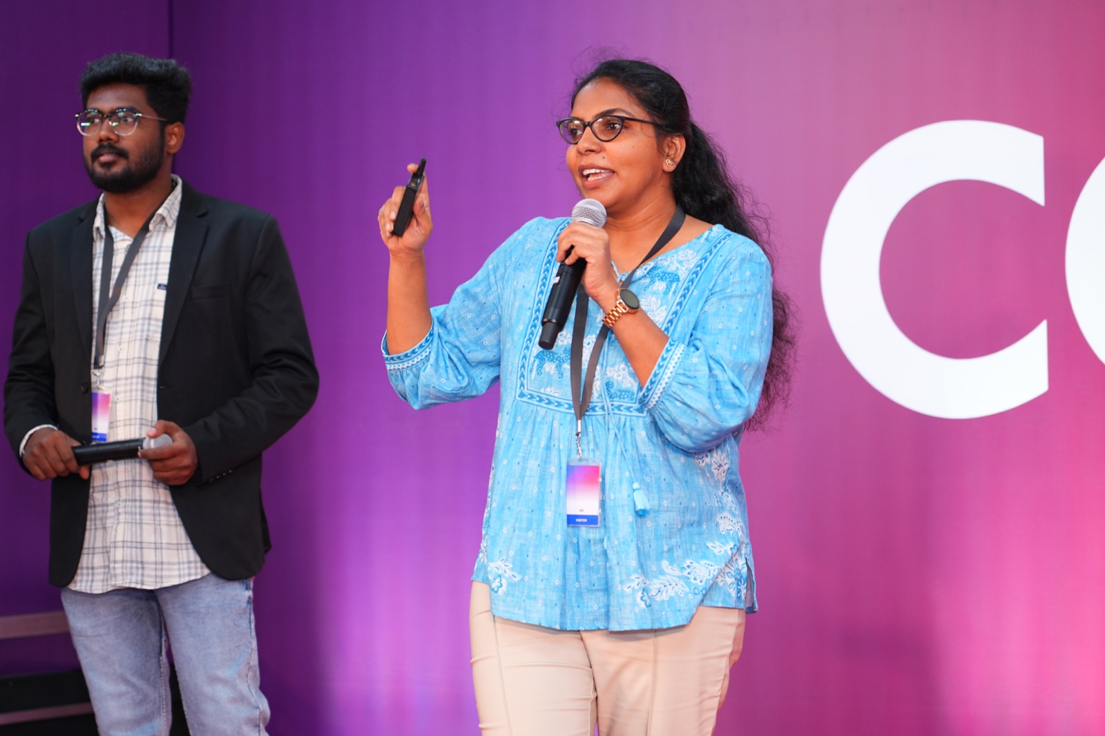 Divya Akula speaking on stage, holding a microphone and presentation remote